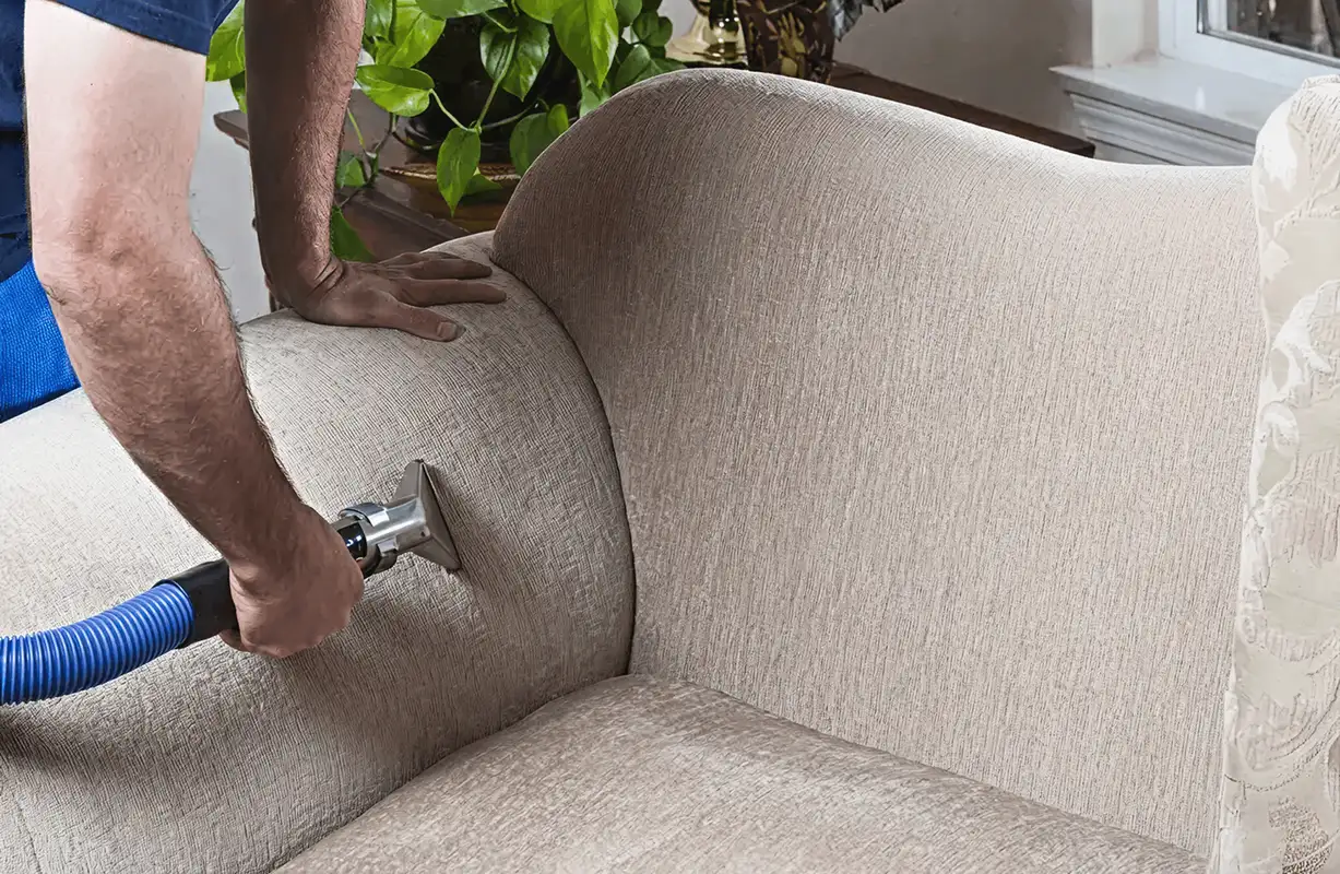 Professional upholstery cleaner deep-cleaning a fabric sofa with a handheld extraction tool and hose, Aurora, CO.